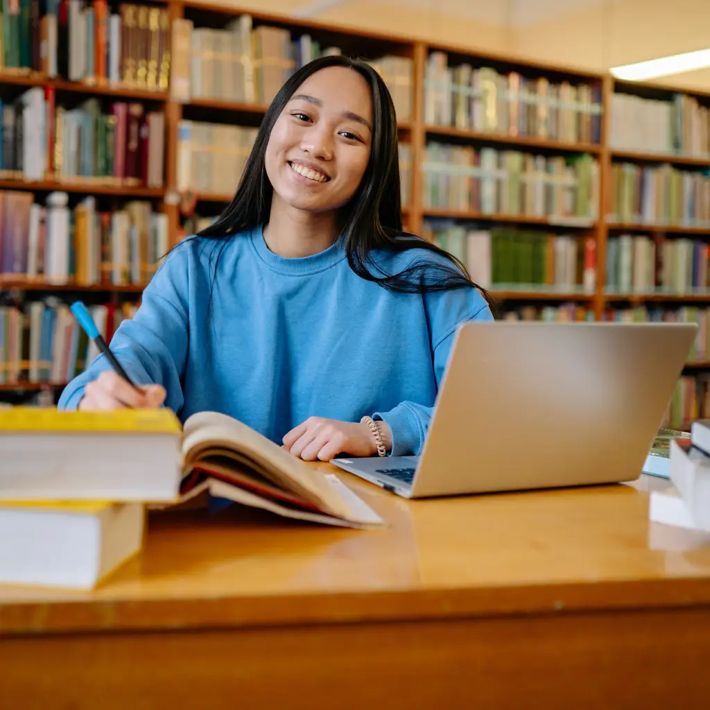 A university student sitting in a library and smiling.